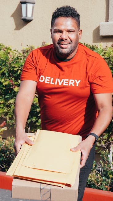 A florist from [COMPANY_NAME], standing outdoors near a neutral-toned building wall and greenery, is holding a beautifully arranged floral gift bouquet prepared for same-day flower delivery. The bouqu